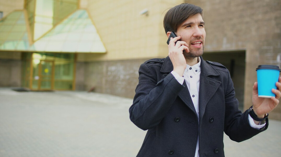 Person answering a phone call at a desk with a laptop